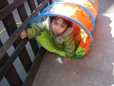 Girl in a play tunnel outside at Early Learners' Nursery School, Leicester